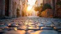 Sunlit cobblestone street in Mediterranean town with warm golden light, historic buildings, and hanging plants creating atmospheric morning or evening ambiance.
