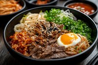 Traditional Korean bibimbap bowl with marinated beef, sunny side up egg, kimchi, bean sprouts, green onions and sesame seeds served in black stone bowl.