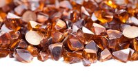 Amber colored glass pieces scattered on white surface create luminous texture with light reflections and transparent glow. Decorative elements for design.