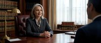Professional middle-aged Caucasian businesswoman lawyer in dark suit smiling during client meeting in traditional law office with leather chair and books.