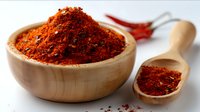 Red chili powder in wooden bowl and spoon with dried chilies on white background, macro food photography for cooking and spicy cuisine concepts.