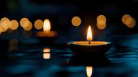 Floating oil lamp with warm flame creates peaceful ambiance against dark blue water surface with golden bokeh lights reflecting in background for meditation.