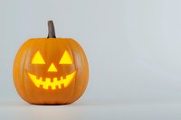 Glowing orange jack o'lantern with classic triangular eyes and zigzag smile carved design on light background, illuminated from within for Halloween decor.