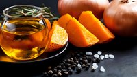 Fresh pumpkin slices with hot herbal tea in glass teapot, black peppercorns and sea salt crystals on dark background, autumn drink composition.