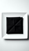 Black folded napkin arranged in geometric pattern on white square plate, overhead view. Minimalist table setting for restaurant, catering, event planning, hospitality design.
