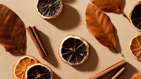 Dried citrus slices, cinnamon sticks and autumn leaves arranged on beige background, creating natural organic composition for seasonal decoration.