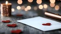 Romantic composition with white paper note, red paper hearts wooden table. Soft bokeh creates intimate atmosphere.