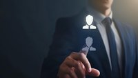 Asian businessman in dark suit pointing at glowing digital human icon, representing HR management, recruitment and talent acquisition in corporate setting.