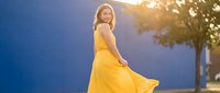 Young woman in flowing yellow dress dancing outdoors at sunset with warm golden light creating dreamy atmosphere for lifestyle and fashion concepts.