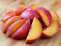 Fresh juicy sliced nectarine segments arranged on wooden cutting board showing bright red skin and yellow flesh, macro food photography.