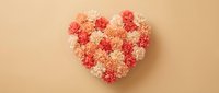 Heart-shaped arrangement of pink and coral carnation flowers on beige background for Valentine's Day, wedding, romance and love celebration.