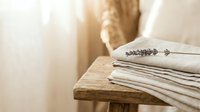 Stack of folded linen towels with lavender sprig on rustic wooden table in bright sunlit bathroom interior for spa and home decor concepts.