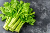 Fresh green celery stalks and leaves arranged on dark stone background, raw organic produce for healthy eating and cooking. Natural food photography.