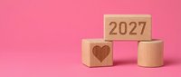 Wooden blocks with 2027 and heart symbol on pink background, representing new year goals, love resolutions, and future planning for design projects.