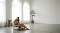 Young mother embracing toddler daughter in minimalist bright living room with natural light streaming through large windows creating peaceful family moment.