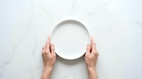 Two hands holding empty white plate on marble surface for food presentation or dining concept.