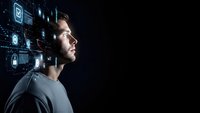 Young Caucasian businessman in profile looking at futuristic digital interface with glowing icons and data visualization on dark background.