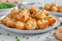 Crispy wontons filled with cream cheese and crab mixture, garnished with fresh chives on white plate. Appetizing party food with dipping sauce.