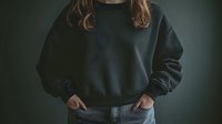 Young woman in oversized dark sweatshirt and jeans with hands in pockets against moody background for casual fashion and lifestyle concepts.