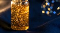 Glass of golden carbonated beverage with bubbles and ice, isolated on dark blue background with bokeh lights, suitable for beverage advertising and product photography.