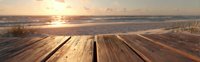 Wooden deck overlooking tranquil beach at sunset, with golden sunlight reflecting on ocean waves and sandy shoreline.