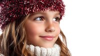 Young Caucasian girl wearing white knitted turtleneck sweater and festive red tinsel hat smiles warmly. Natural makeup, blue eyes and long blonde hair create cheerful winter holiday mood.