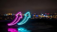Neon arrow signs glowing pink and cyan against dark urban skyline at night creating vibrant light display for business growth and success concepts.
