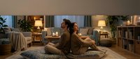 Couple sitting back-to-back on floor in cozy living room with warm lighting, comfortable furniture, and plants. Suitable for lifestyle, relationships, home decor, and interior design content.