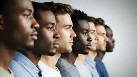 Diverse group of professional men in business attire standing in profile line formation showing teamwork and leadership in modern corporate environment.