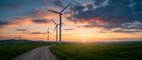 Wind turbines on green hills at sunset with dramatic sky and dirt road leading through renewable energy farm for sustainable power generation.