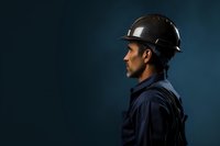 Side profile of construction worker wearing black hard hat and navy uniform against dark blue background, representing industrial safety and professionalism.