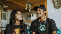 Young Asian couple laughing together in cozy home setting with wooden ceiling and bohemian decor, creating warm atmosphere of joy and connection.