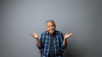 Senior man with gray hair and dark skin, wearing blue plaid shirt, gesturing with open palms in welcoming or uncertain pose against neutral gray background for portrait and lifestyle use.