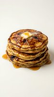 Stack of golden-brown pancakes with melting butter and maple syrup dripping down sides, perfect for breakfast and food photography projects.