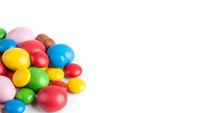 Colorful candy eggs scattered on white background for Easter celebration and spring holiday decorations.