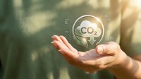 Hands holding a glowing CO2 reduction icon with green leaves, symbolizing carbon neutrality and eco-friendly environmental sustainability concept.