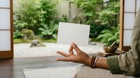 Cropped view of person holding blank white card with zen garden and lush greenery visible through glass doors behind, suitable for mockups and advertising campaigns.