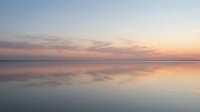 Serene sunset over calm water with soft pink and orange hues reflecting on glassy surface, creating tranquil landscape for relaxation and wellness content.