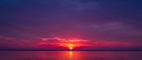 Vibrant sunset over calm water with golden sun reflecting on surface, dramatic purple and pink sky, serene landscape for travel and nature projects.