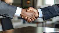 Close-up of business handshake between diverse professionals in formal suits, symbolizing partnership agreement and successful deal completion in office setting.