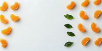 Fresh mandarin orange segments scattered with green leaves on white background, creating minimal food composition for healthy eating concept.