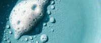 White soap foam and water droplets on a blue surface, close-up texture background for skincare, beauty, and hygiene product design.