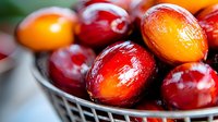 Fresh ripe oil palm fruits in metal basket, vibrant red and orange colors with natural sheen, macro food photography showing texture and detail.