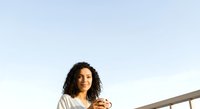 Young woman with curly dark hair and medium skin tone wearing casual beige shirt, looking thoughtful against clear sky background for lifestyle and portrait use.