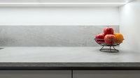 Minimalist kitchen counter with gray backsplash and metal fruit bowl holding red apples and orange citrus. Modern interior design for home decor, culinary, and lifestyle projects.