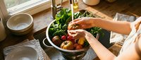 Woman preparing fresh organic salad with mixed greens and vegetables in rustic kitchen setting for healthy meal preparation and cooking lifestyle.