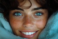Close up portrait of young woman with bright blue eyes, natural freckles, and radiant smile against turquoise background, expressing joy and authenticity.