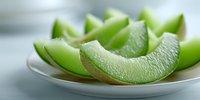 Fresh slices of green honeydew melon on white plate, juicy and refreshing summer fruit with water droplets on surface.