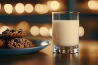 Fresh glass of milk next to homemade chocolate chip cookies on blue plate against warm bokeh background, creating cozy evening atmosphere for comfort food concept.