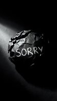 Crumpled black paper ball with the word Sorry written in chalk on dark background, symbolizing regret, apology, and emotional conflict.